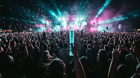 Menschenmenge bei einer Open-Air-Veranstaltung nachts, eine Hand hält ein türkises Wassereis hoch